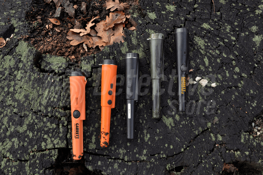 Five hand-held metal detectors on a tree stump, among moss and dry leaves.
